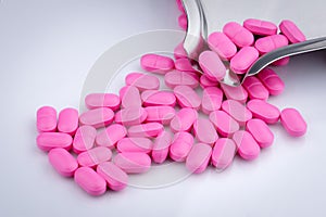 Pile of pink tablets pill on white background near stainless steel drug tray. Norfloxacin 400 mg for treatment cystitis