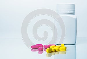 Pile of pink and yellow tablets pills near plastic pills bottle with blank label isolated on white background with copy space.