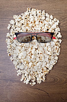 A pile of popcorn in the shape of a head and 3D glasses for watching movies on a wooden background