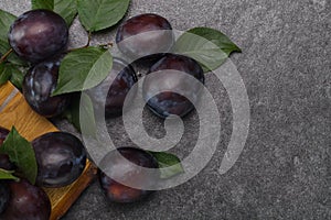 Pile of purple plums with leaves on stone table