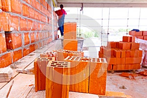 Pile of red blocks on wooden platform, worker build wall with bricks and mortar