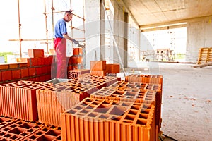 Pile of red blocks, worker builds wall with bricks and mortar, building site