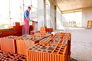 Pile of red blocks, worker builds wall with bricks and mortar, building site