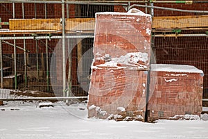 Pile of red building construction bricks under winter snow in england uk