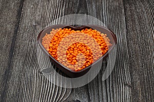 Pile red lentil in shape of heart isolated on wooden background. Top view. Flat lay.