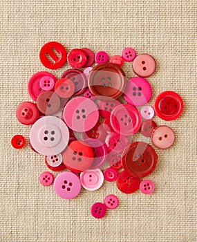 Pile of red and pink buttons on hessian