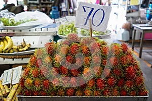 Pile of ripe sweet reddish rambutan fruit with pliable green hair in local market atmosphere