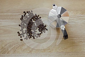 Pile of roasted brown coffee beans on the light wooden surface of the table and a geyser coffee maker, top view