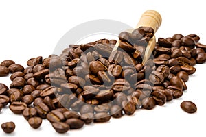 Pile of roasted coffee beans with wooden scoop on white background, selective focus