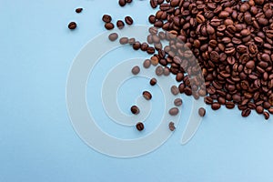 Pile of roasted dark brown coffee beans on blue background with copy space. Aroma drink concept.