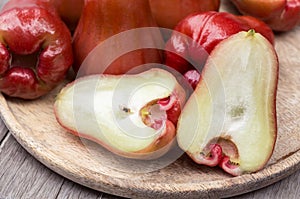 A pile of rose apples with a slice in a wooden tray on the table