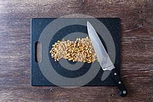 Pile of rough chopped walnuts on a black cutting board, chef knife, on dark wood table