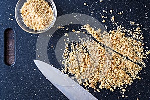 Pile of rough chopped walnuts on a black cutting board, fine chopped walnuts in glass bowl, chef knife