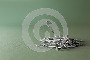 Pile of safety pins on green background, space for text