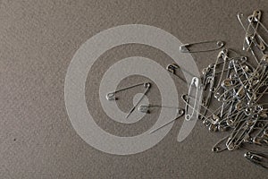 Pile of safety pins on grey textured background, flat lay. Space for text