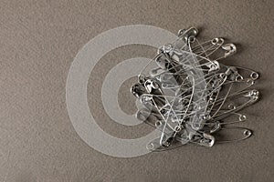 Pile of safety pins on grey textured background, flat lay. Space for text