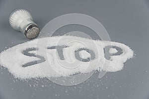 A pile of salt from salt shaker, lettering with word stop salt, concept excessive salt intake