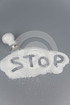 A pile of salt from salt shaker, lettering with word stop salt, concept excessive salt intake