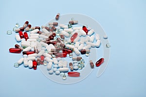 Pile of scattered pills, translucent capsules and medical dragees scattered on blue background. Pharmaceutical industry