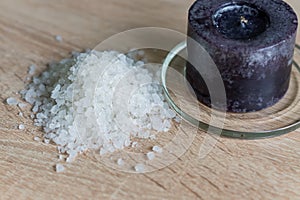 Pile of sea salt and black candle on wooden table. Natural ingredient for spa and exfoliation