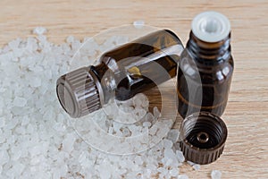 Pile of sea salt and bottles with aromatic oil on wooden table. Natural ingredient for spa and exfoliation