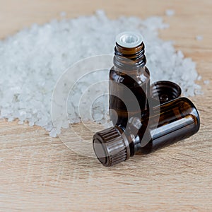 Pile of sea salt and bottles with aromatic oil on wooden table. Natural ingredient for spa and exfoliation