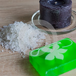 Pile of sea salt, soap bar and black candle on wooden table. Natural ingredient for spa and exfoliation