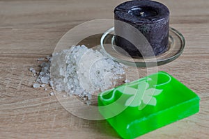 Pile of sea salt, soap bar and black candle on wooden table. Natural ingredient for spa and exfoliation