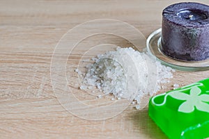 Pile of sea salt, soap bar and black candle on wooden table. Natural ingredient for spa and exfoliation. Copy space