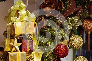 Pile of shiny gift boxes decorated in Christmas tree with Christmas ornament decorations in the background.