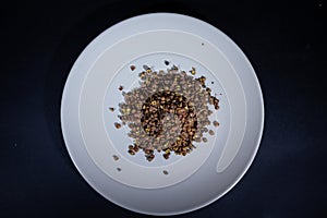 pile of Sichuan pepper on a white plate on a black background. it\'s a chinese spice called Szechuan pepper, Szechwan