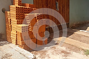 Pile of six-hole bricks on the floor, leaning against the wall next to the rusty orange gate photo