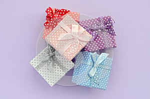 Pile of a small colored gift boxes with ribbons lies on a violet background. Minimalism flat lay top view