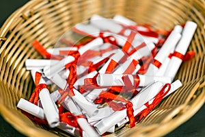 Pile of small paper scrolls in wicked basket. White scrolls tied with red ribbon. Future prediction, advice or sig