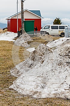 Pile of snow on brown grass ground with house, van and people in the background in winter in Hokkaido, Japan