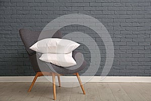 Pile of soft bed pillows on armchair near brick wall