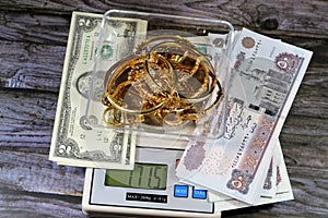 Pile stack of gold on a digital accurate scale in grams, bracelets with Egyptian EGP pounds and American dollars money, gold price