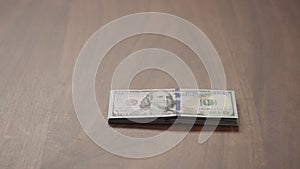 Pile stack of hundred dollar bills on walnut table slide shot