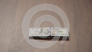 Pile stack of hundred dollar bills on walnut table slide shot