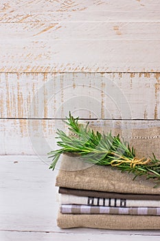 Pile of stacked folded kitchen towels on white plank wood background, rosemary twig, rustic minimalistic style