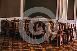 A pile of stacked wooden chairs lie on top of each other, standing in the corner of the room of the old house