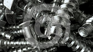 Pile of steel chrome screws rotating on black background. Stainless steel bolts, metal anchor bolts on the table. Helix