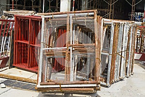 A pile of steel scaffolding with brown rust on the cocrete floor in front the building