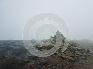 Pile of stones on the muddy ground surrounded by mist on the top of Hoverla peak in Carpathian Mountains