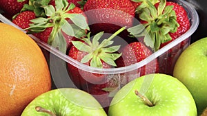 Pile of strawberries in plastic bowl surrounded with fruits and vegetables