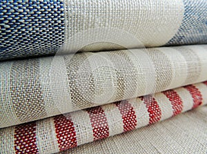 Pile of striped white grey blue red linen cotton fabrics on white background.