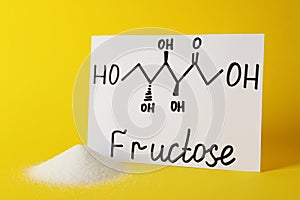 Pile of sugar and word Fructose with drawn scheme on paper against yellow background