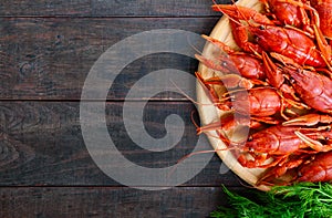 A pile of tasty boiled crawfish on a round wooden tray on a dark table. Top view.