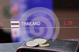 Pile of Thai baht coins on THB on black wallet with black floor and digital board of currency exchange money background.