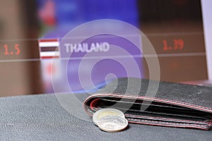 Pile of Thai baht coins on THB on black wallet with black floor and digital board of currency exchange money background.